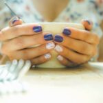 A woman with colorful nails holds a mug, capturing a moment of warmth and style indoors.
